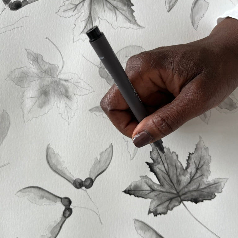 Hand holding a pen over a pattern of leaves and insects on a white background